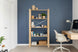 Estante Legno de madeira clara com objetos decorativos e livros em um home office moderno. Ao lado, uma bancada flutuante com cadeira branca e luminária. Ambiente organizado, funcional e acolhedor.