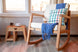 foto ambientada cadeira de amamentacao com balanco comodita jatoba e bege em jardim interno vista de frente com manta e almofada sobre ela e banco ao lado
