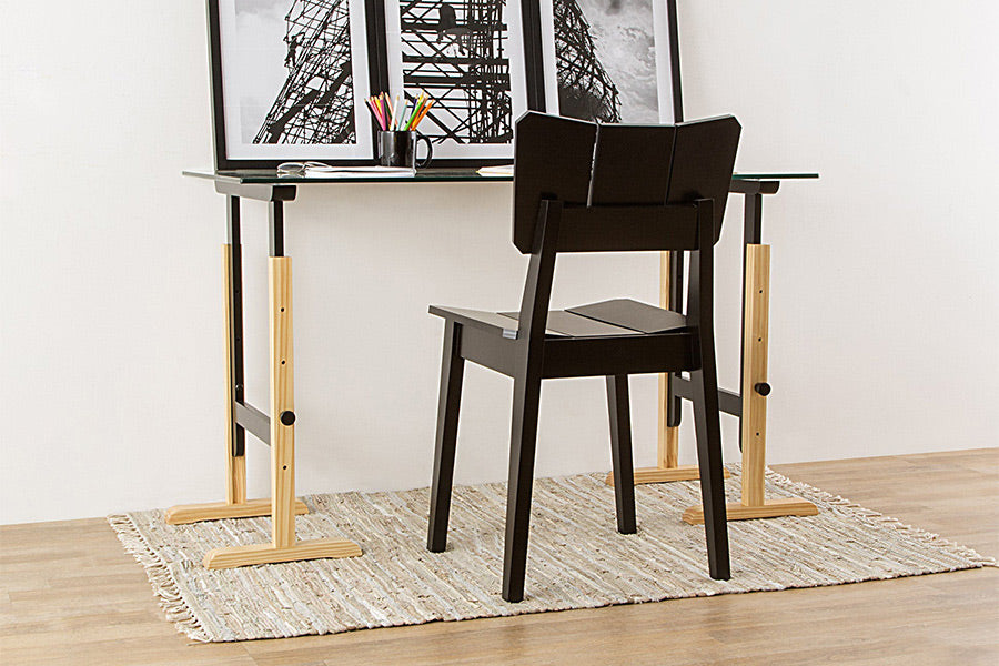 ambiente com cadeira de madeira uma preta vista de tras em frente de uma escrivaninha com quadros sobre ela