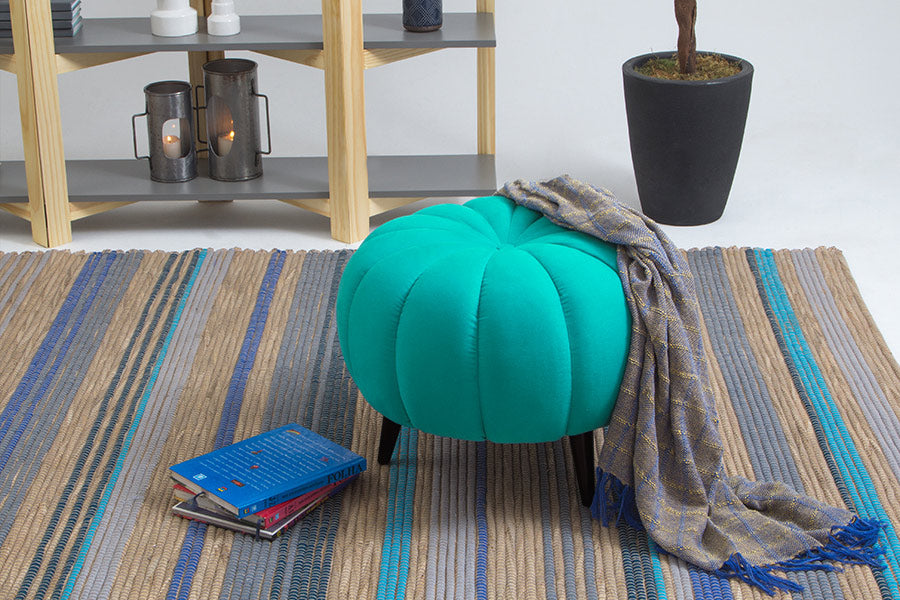 ambiente com puff redondo pitanga turquesa com tapete colorido e livro ao lado