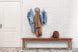 foto ambientada banco móveis 200 bertioga jatobá em hall de entrada com parede branca atrás e cabideiro com roupas acima