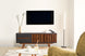 foto ambientada de sala de estar com rack laqueado para tv 1,65 m panteon grafite visto de frente com objetos sobre rack e tv fixada na parede