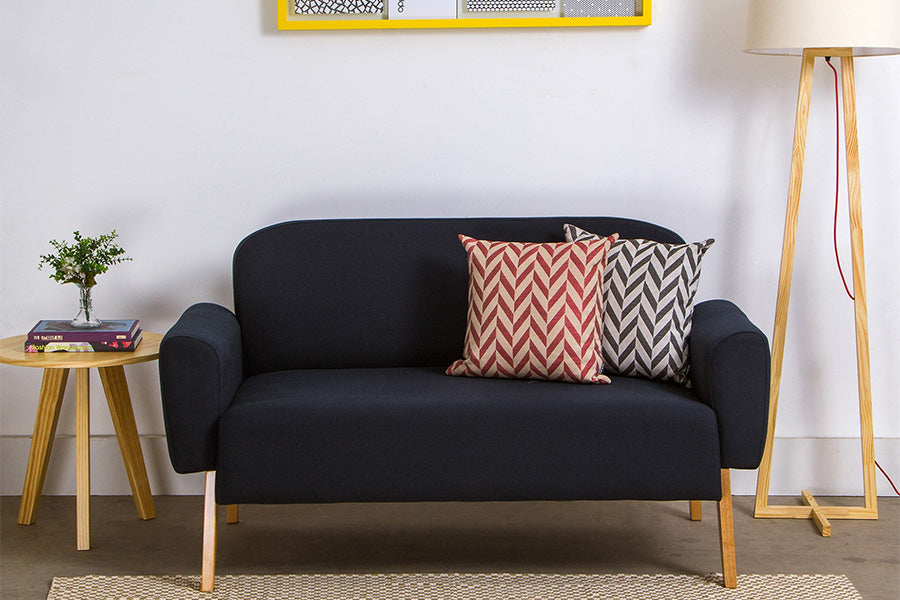 foto ambientada sofa dois lugares agnes azul ao lado de uma mesa lateral com uma mesa lateral cru e uma almofada vermelha